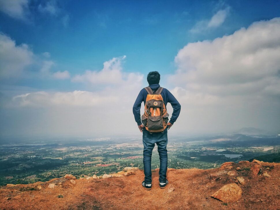 https://www.pexels.com/photo/man-in-blue-dress-shirt-and-blue-jeans-and-orange-backpack-standing-on-mountain-cliff-looking-at-town-under-blue-sky-and-white-clouds-732629/